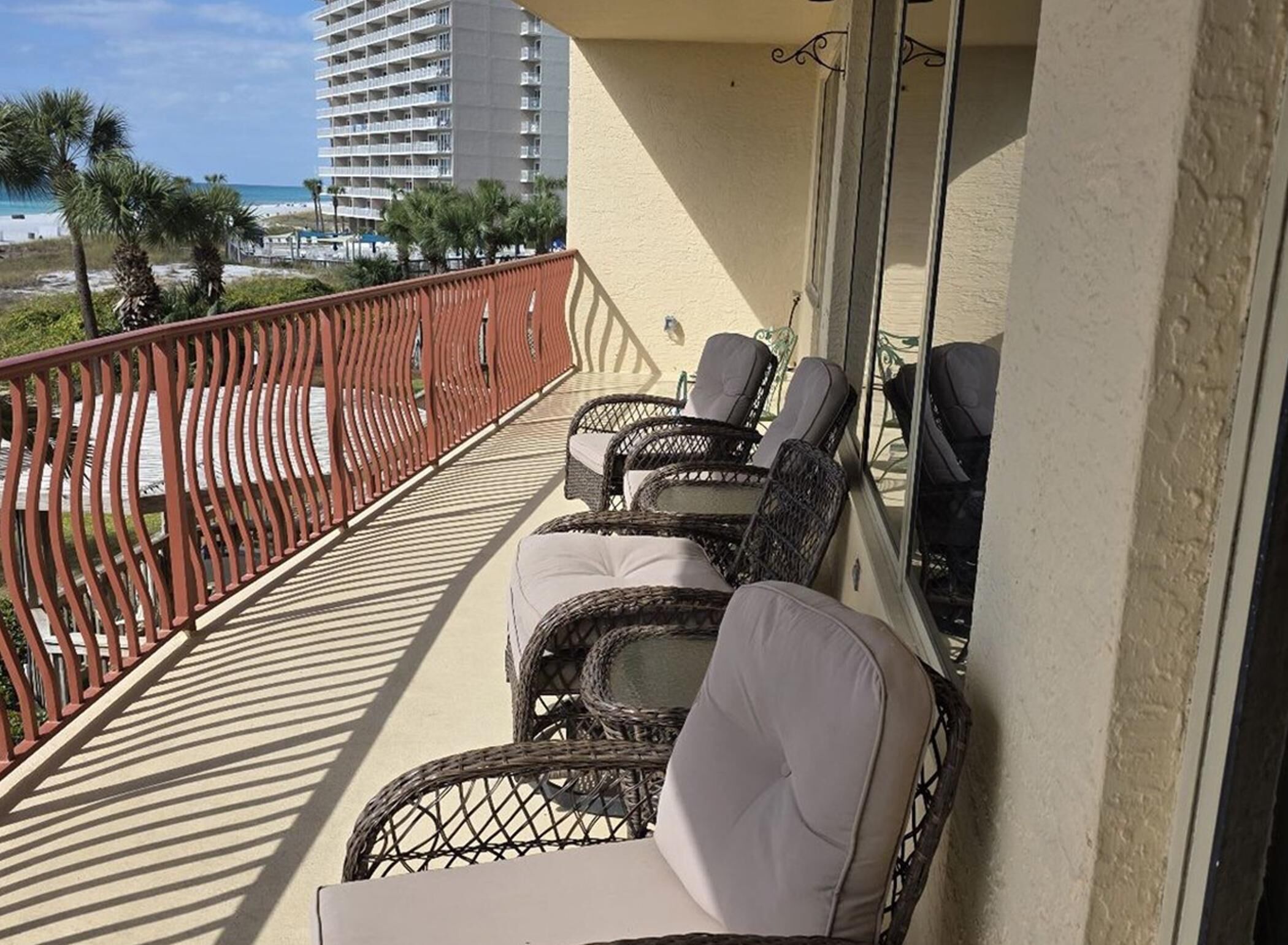 A balcony with wicker chairs and a view of the beach and hotel buildings.