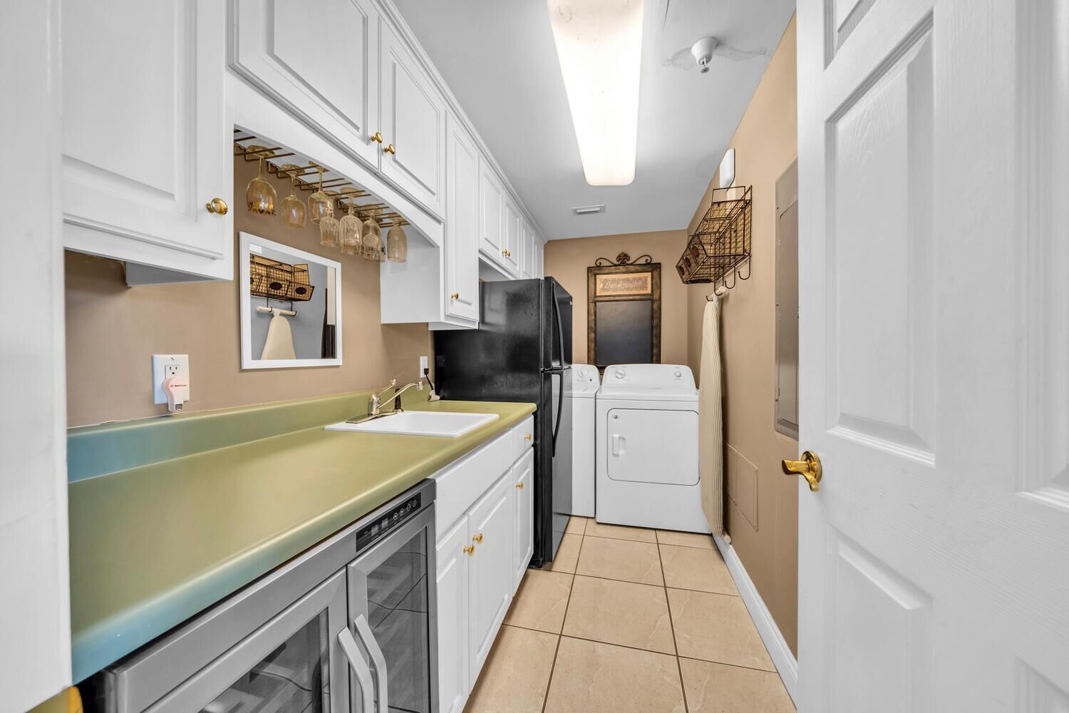 Una cocina compacta con armarios blancos, una encimera verde, un refrigerador negro y una lavadora.