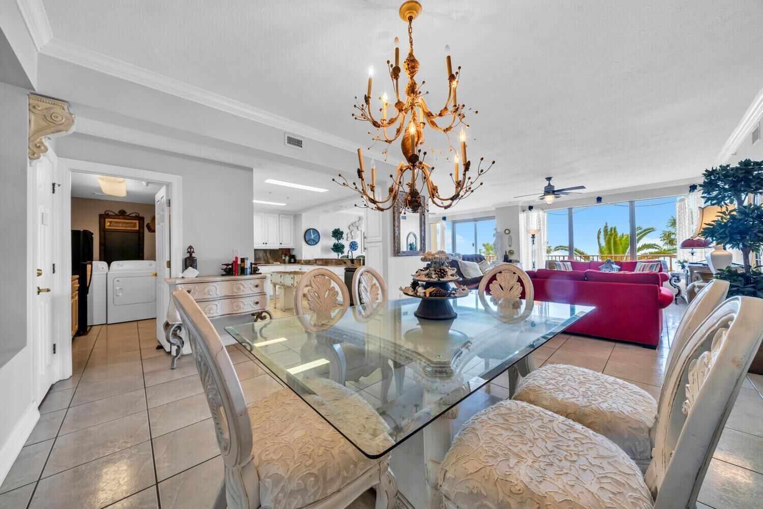 A spacious living area with a glass dining table, elegant chairs, a chandelier, and a red sofa.