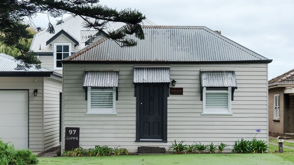A two-story house with a dark front door, white window shutters, and a small porch. - The Dog House Cottage (Port Fairy)