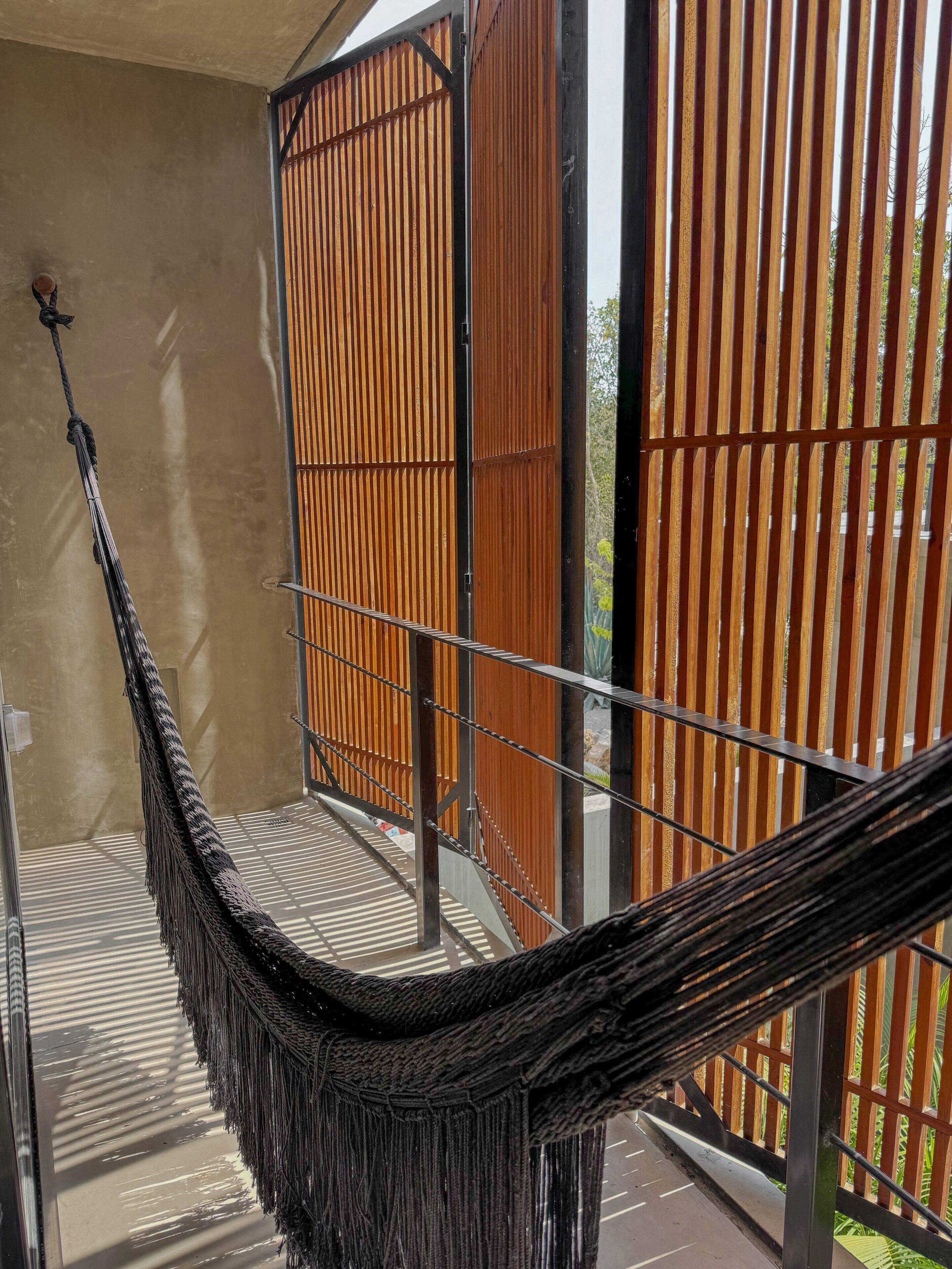 A hammock on a balcony with a view of a wooden fence and a building in the background.