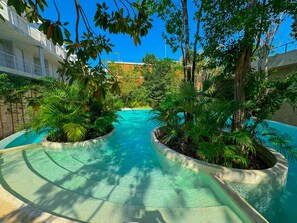 A pool area with two curved water features surrounded by lush greenery and trees. - Tu refugio ideal Seremonia 206 (Tulum)