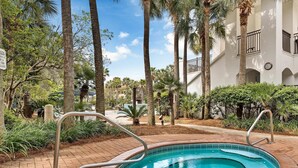 A swimming pool with metal railings, surrounded by palm trees and a brick pathway. - Blue Turtle Dreams (Destin)