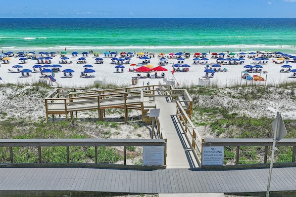 A beach with a wooden boardwalk leading to a private beach area, marked by a sign indicating no trespassing.