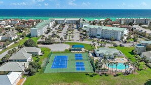 Un resort con varias canchas de tenis, piscina y vistas a la playa.