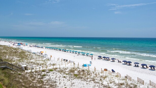 A beach with rows of umbrellas and beach chairs, a wooden fence, and a staircase leading down to the beach. - Gulfview II 218 (Miramar Beach)