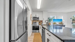 A modern kitchen with stainless steel appliances, a large island with a black countertop, and a view of the beach through the window. - Gulfview II 218 (Miramar Beach)