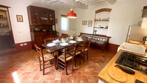 Comedor con una mesa de madera dispuesta para cuatro personas, rodeada de sillas con asientos de fibras tejidas. Una lámpara colgante roja ilumina la mesa.
