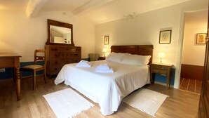 Un dormitorio ordenado con una cama, un tocador, una silla y dos mesitas de noche con lámparas.