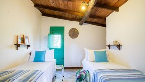 Una habitación con dos camas, techo de madera, una puerta verde y un taburete pequeño.