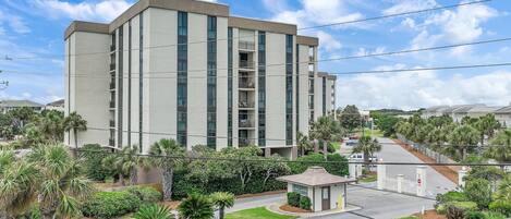 A multi-story building with a flat roof, surrounded by well-maintained greenery and a clear sky.