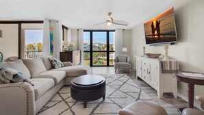 A modern living room with a large window, a ceiling fan, a sofa set, a coffee table, and a television mounted on the wall. - Enclave 302b (Destin)