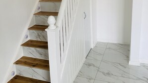 Una escalera con barandillas blancas y peldaños de madera que conduce a una habitación con paredes blancas y suelo de mármol.