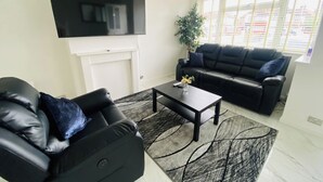 Una sala de estar con un sofá de cuero negro, una mesa de centro negra y un televisor montado en la pared.