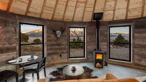 A rustic cabin interior with a stone fireplace, wooden walls, and large windows offering mountain views. - Mountain Yurt: Luxe Yellowstone Cabin | Condé Nast (Emigrant)