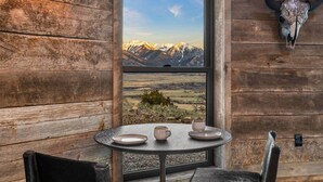 A rustic wooden interior with a table set for two, a mountain view through a window, and a mounted skull on the wall. - Mountain Yurt: Luxe Yellowstone Cabin | Condé Nast (Emigrant)