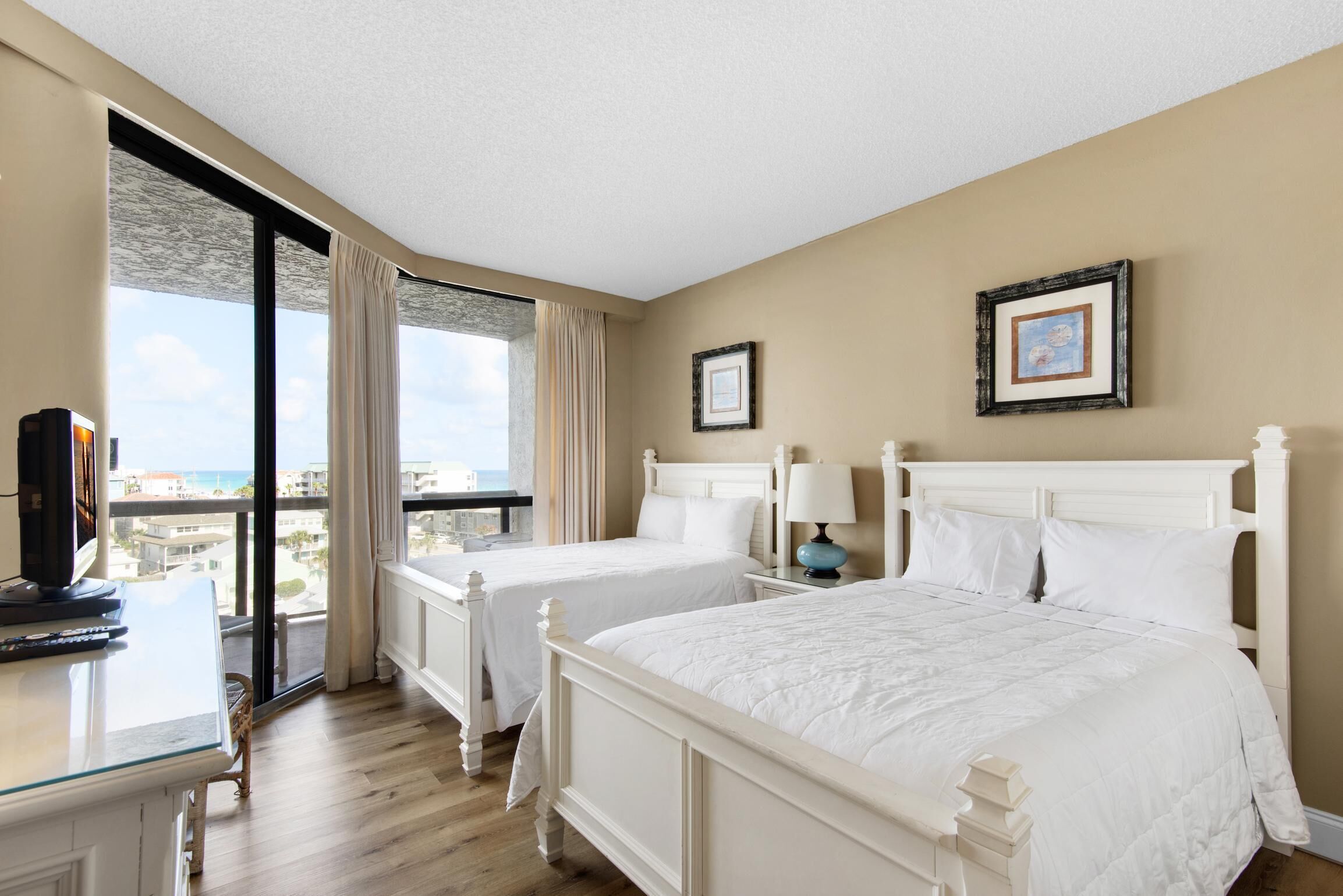 Habitación de hotel con dos camas, un escritorio con ordenador y ventanas amplias con vistas a la ciudad.