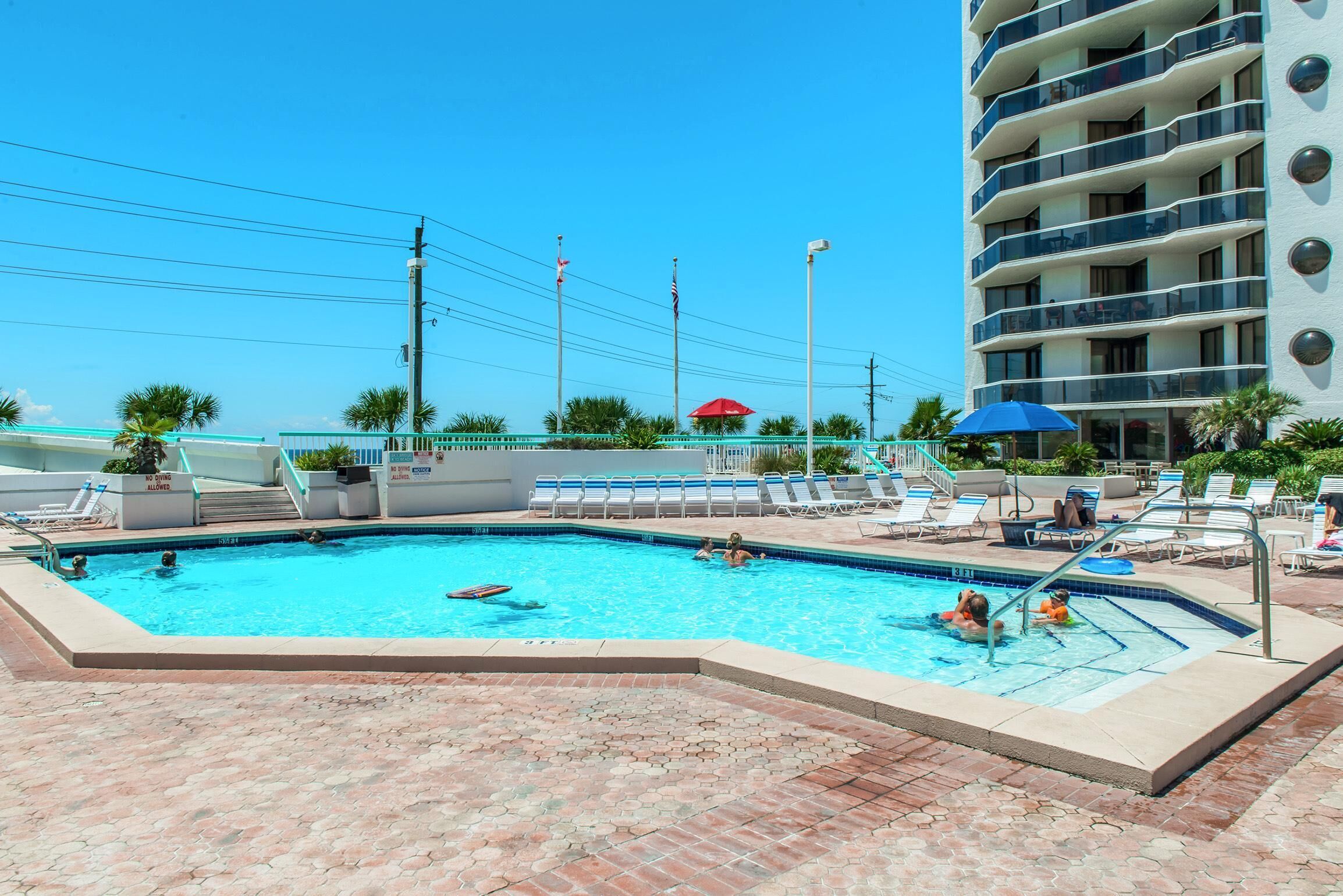 A swimming pool with lounge chairs and umbrellas, surrounded by a brick patio.
