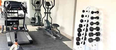 A gym with treadmills, stationary bikes, and a rack of dumbbells.
