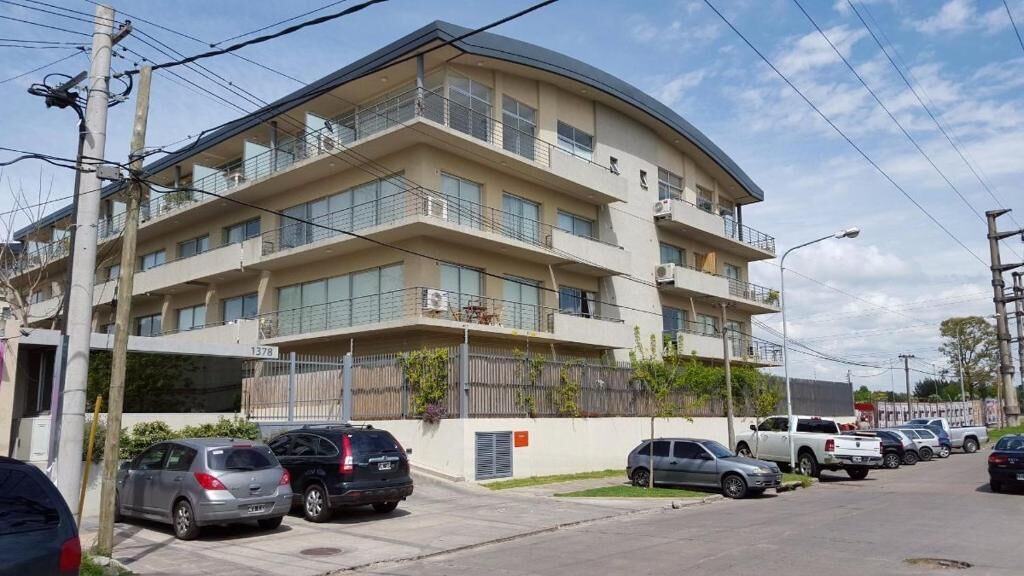 Un immeuble à plusieurs étages doté de balcons, avec des voitures garées et des unités de climatisation visibles.