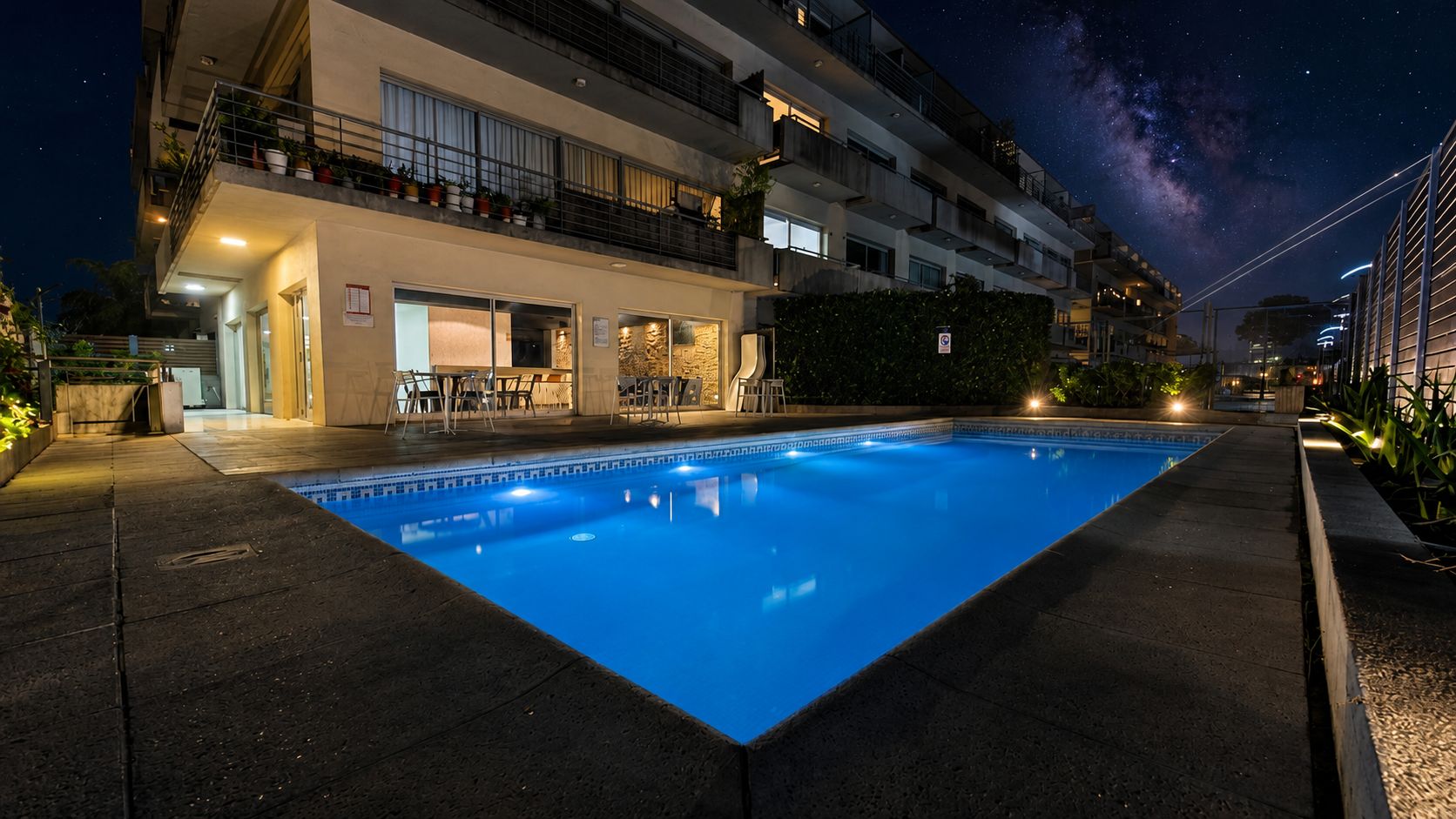 A swimming pool with a clear night sky and a building with balconies in the background.