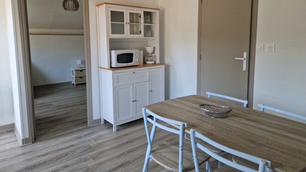 Een kamer met een houten eettafel, witte kasten en een magnetron.