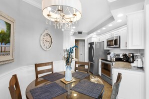 A modern kitchen with white cabinetry, stainless steel appliances, and a dining area with a wooden table and chairs.
