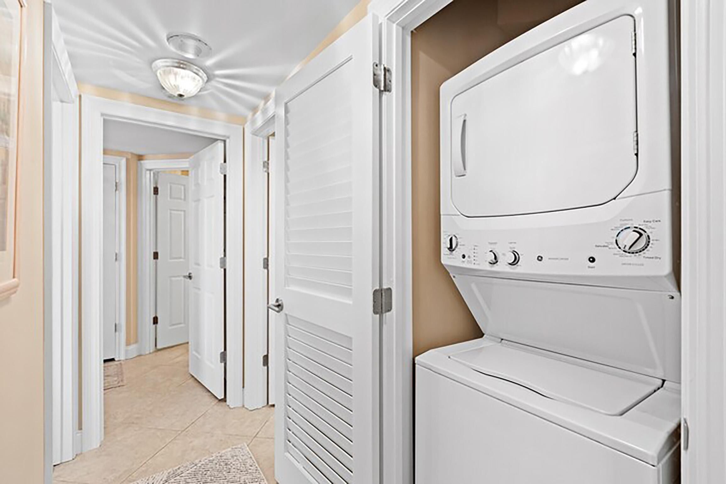 A laundry room with a front-loading washer and dryer, beige walls, and a tiled floor.