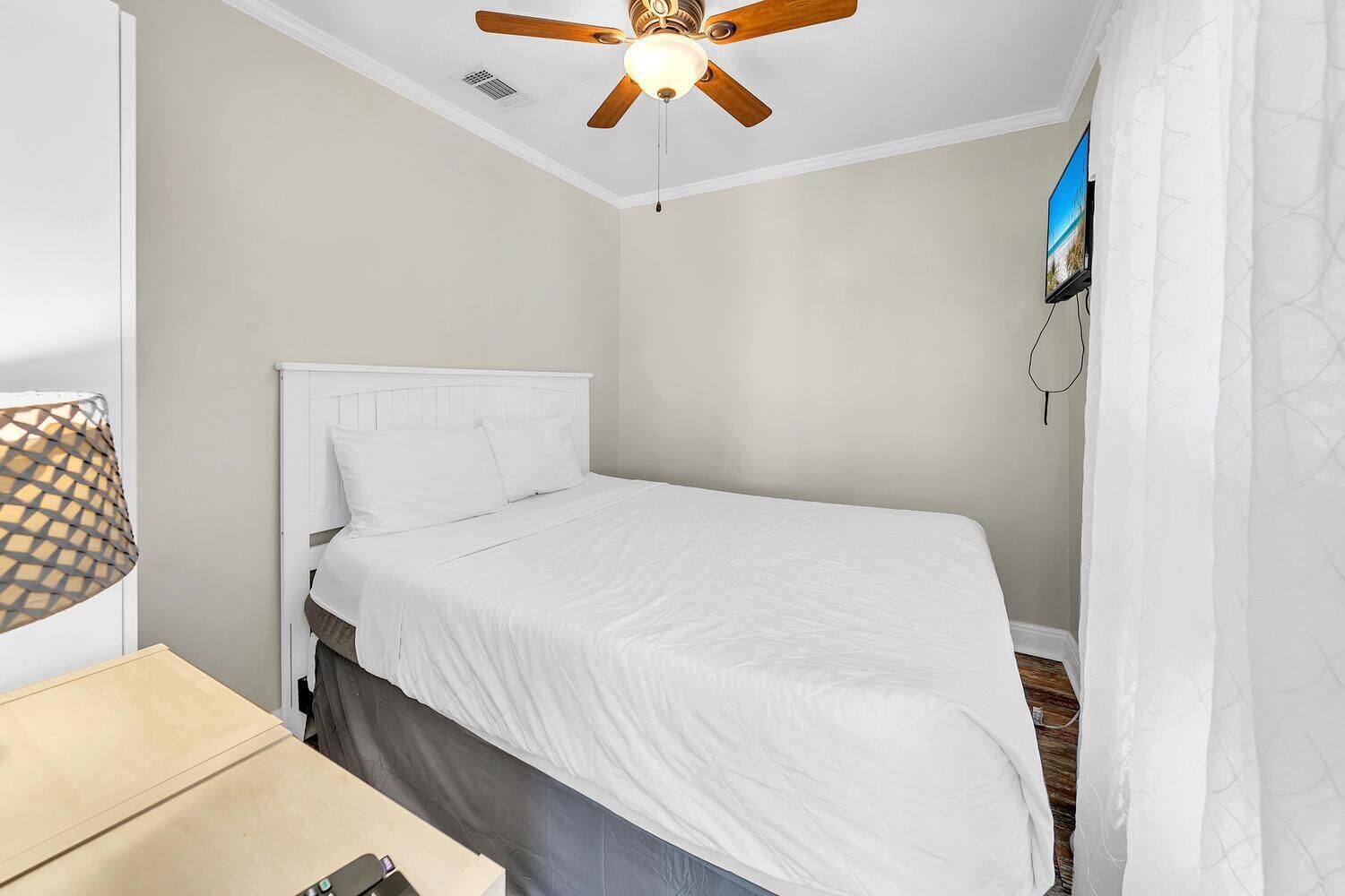 A single bed with a wooden headboard, a ceiling fan, and a TV mounted on the wall.