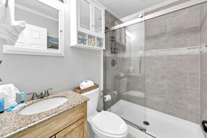A bathroom with a granite countertop, a white sink, a toilet, and a glass-enclosed shower. - Misty Harbour 7 (Panama City Beach)