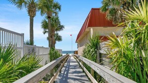 A wooden boardwalk leading to a building with a red roof, surrounded by palm trees and a white fence. - Misty Harbour 7 (Panama City Beach)