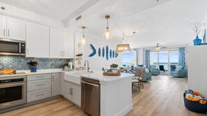A modern kitchen with white cabinetry, stainless steel appliances, and a large island. - Beach Colony West 4B (Pensacola)