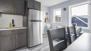 Une cuisine moderne avec des meubles gris, un réfrigérateur en acier inoxydable et un coin repas comprenant une table et des chaises.