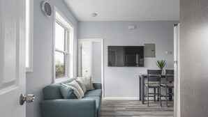 Un salon moderne avec un canapé de couleur turquoise, un coin repas comprenant une table et des chaises, et une cuisine équipée d’un four à micro-ondes et de placards.
