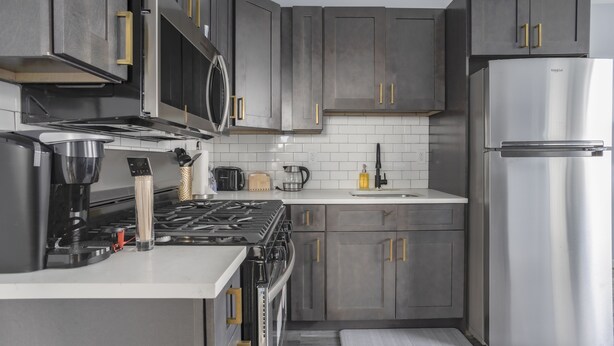 Une cuisine moderne avec des meubles gris, des appareils en acier inoxydable et un plan de travail blanc.