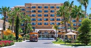 A multi-story hotel with balconies, a central entrance, and a small vehicle in the foreground. - Deluxe 2 BR, 3 Bath, sleeps 6, Ocean Front, Jacuzzi. Ready for Bisbee Tournament (Cabo San Lucas)