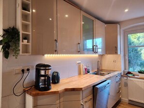 Een moderne keuken met witte kastjes, een houten aanrecht, een koffiezetapparaat, een waterkoker en een vaatwasser.