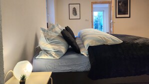 Un dormitori amb llit, almoinades, una làmpada de nit i una porta que dona a una altra habitació.