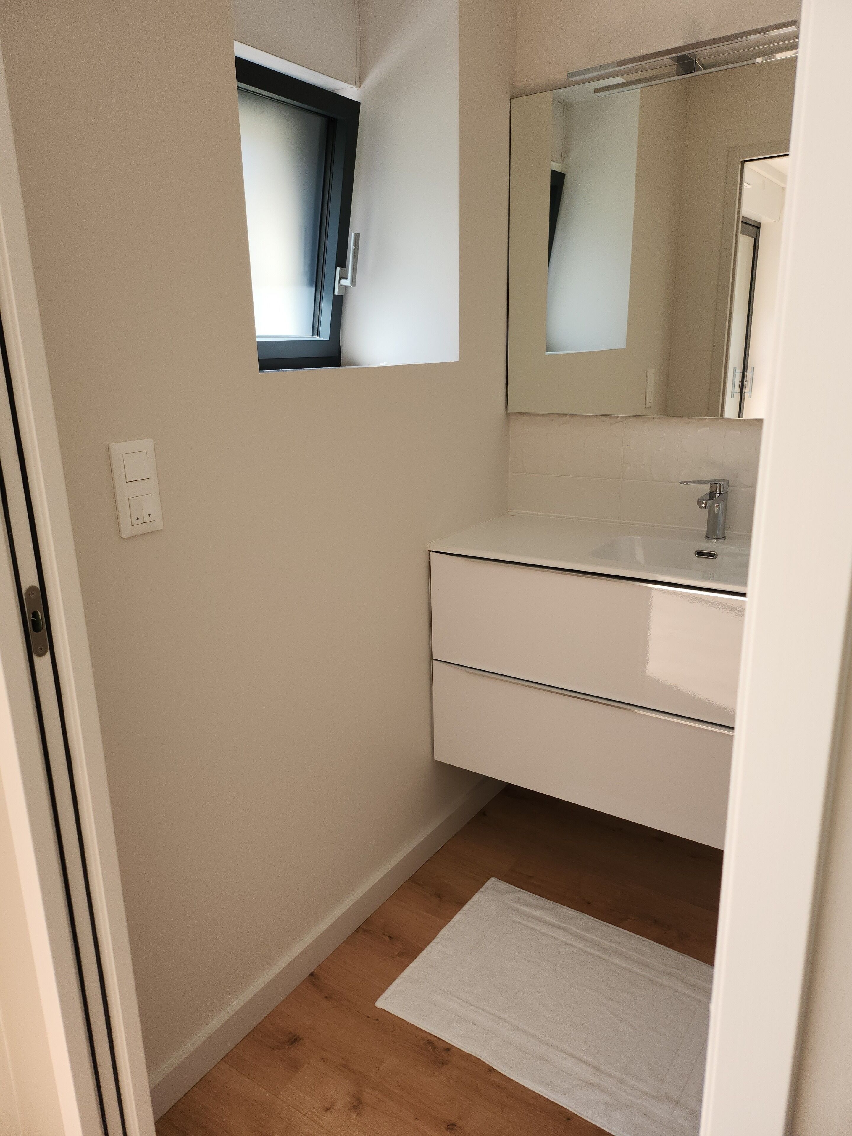 A small, clean bathroom with a white vanity, a mirror, and a wooden floor.