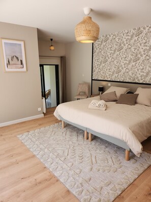 Quarto com uma cama grande, luminária pendente de vime, parede estampada e quadro na parede.