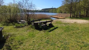 A grassy area with a wooden bench and picnic table, a wooden dock extending into a lake, and trees surrounding the area. - Ferienwohnung Direkt am See (Wokuhl-Dabelow)