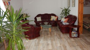 A living room with a wooden ceiling, a leather sofa set, a glass coffee table, and a bookshelf. - Ferienwohnung Direkt am See (Wokuhl-Dabelow)