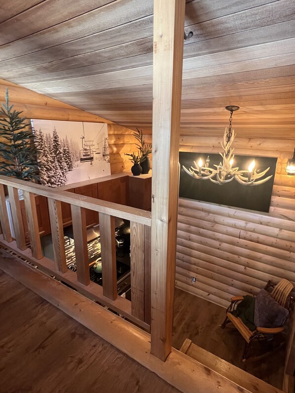 A wooden cabin interior with a balcony, a dining area, and a chandelier.