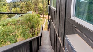 Un escalier en bois mène à une fenêtre donnant sur une zone boisée, avec des maisons visibles au loin.