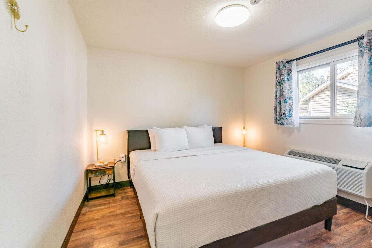 A bedroom with a bed, bedside lamps, a window with curtains, and a wall-mounted heater.