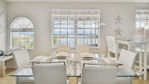 A dining area with a glass table, white chairs, and a view of the city through large windows.