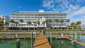 A multi-story hotel with a central atrium, a wooden dock leading to a marina, and palm trees in the foreground.