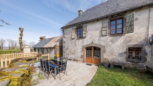 Une maison de campagne en pierre, dotée d’un patio carrelé, d’une clôture en bois et surplombant un ciel dégagé.
