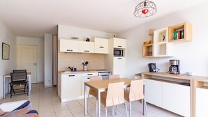 Cocina moderna con armarios blancos, microondas y cafetera. Hay una mesa de comedor con sillas y una pequeña zona de estar con una silla y una cama.