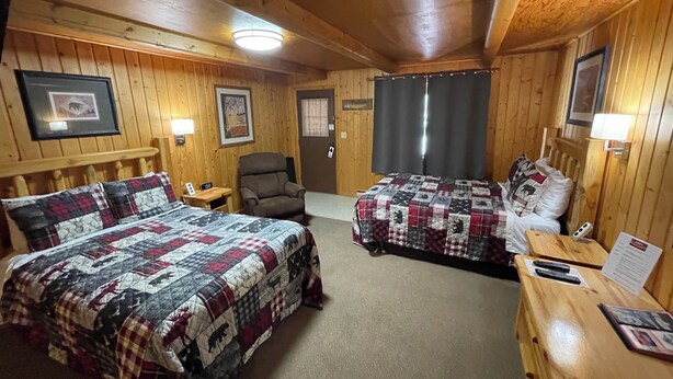 A wooden cabin room with two beds, a chair, a desk, and a nightstand. - Lodge Room #7 - Montana Mountain Views (Butte)